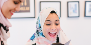 A woman wearing a hijab looking excitedly at her phone